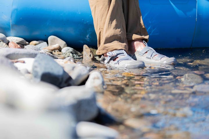 Man wearing Oboz Whakata Off Road sandals in the river next to a raft.