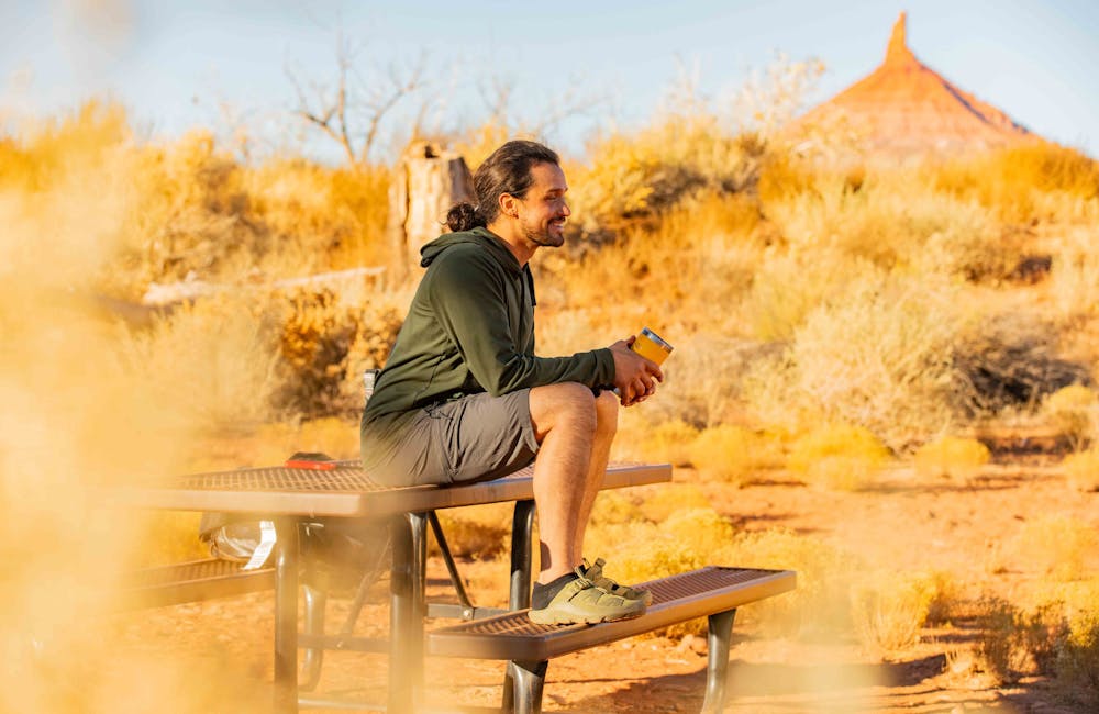 Man wearing Oboz Whakata Ease casual sandal in Conifer while drinking coffee on a bench in Moab, Utah.