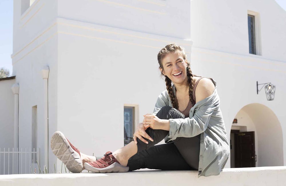 Woman sitting on a wall next to a historic church while wearing Oboz Whakata Town casual sandals.
