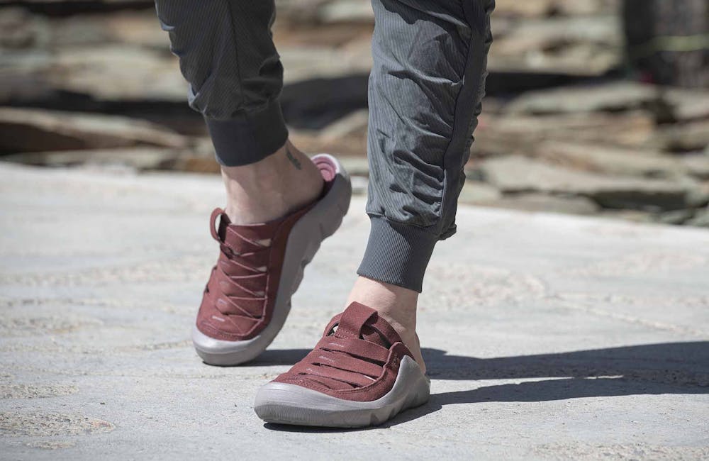 A woman wearing a pair of Oboz Whakata Town casual sandals while walking on a path.