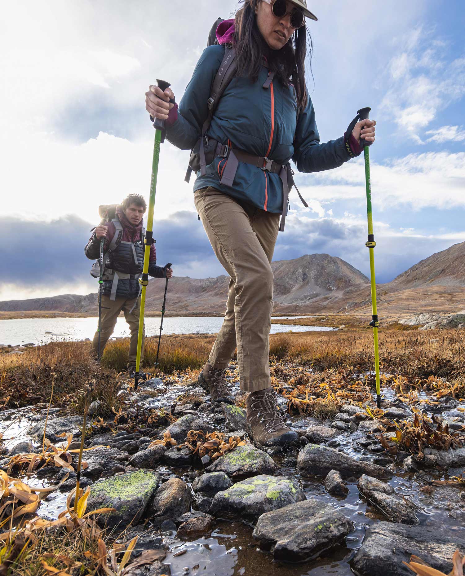 Two hikers cross a stream in waterproof Oboz hiking boots.