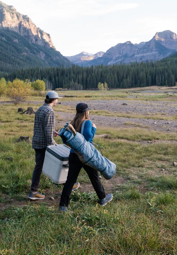 Two people walking down a trail with things for a picnic.