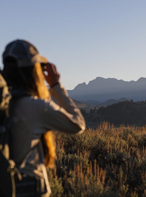 Woman looks at a mountain vista through a pair of binoculars.