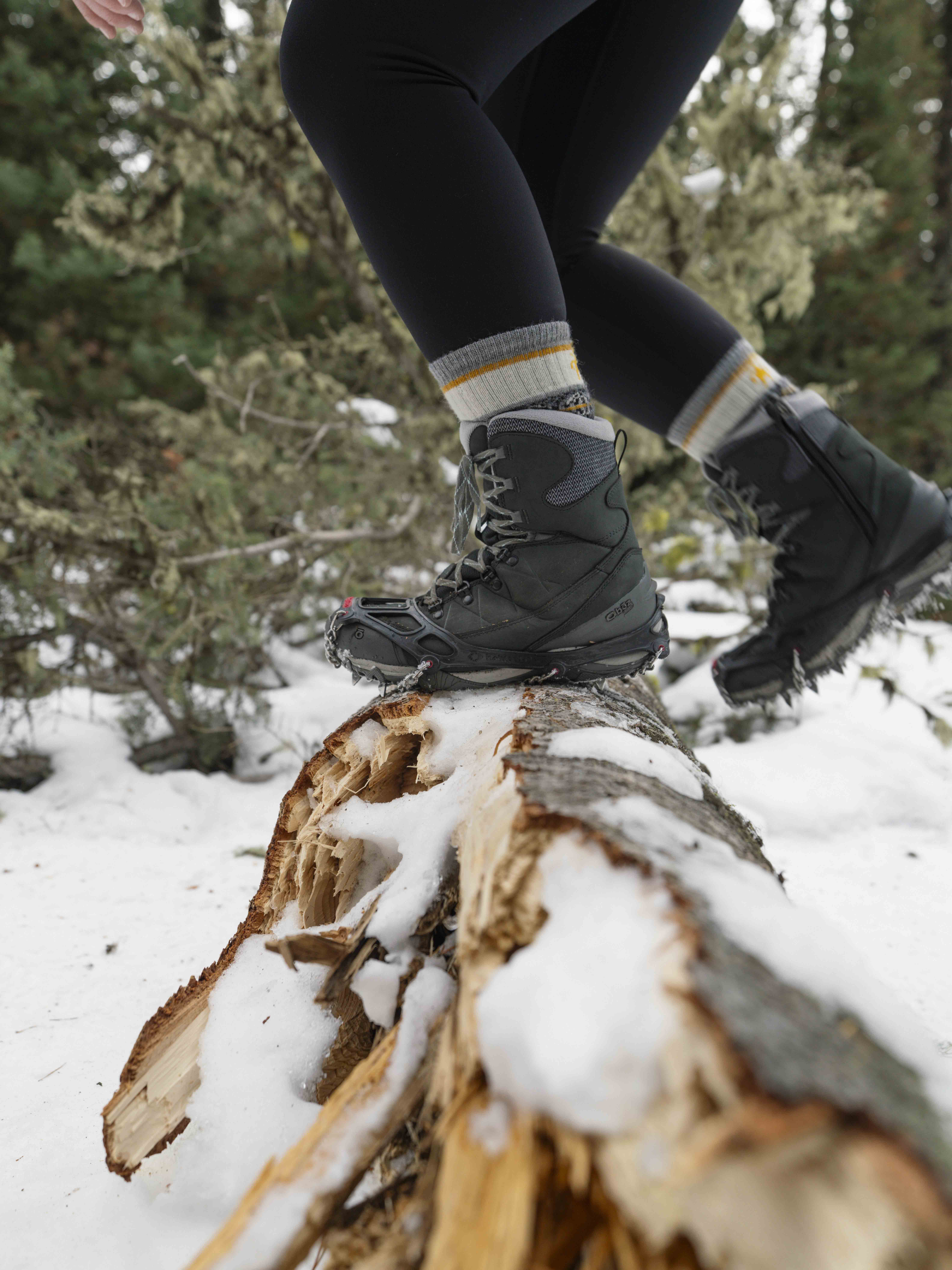 Hiker stepping over a log while hiking in snowy terrain.