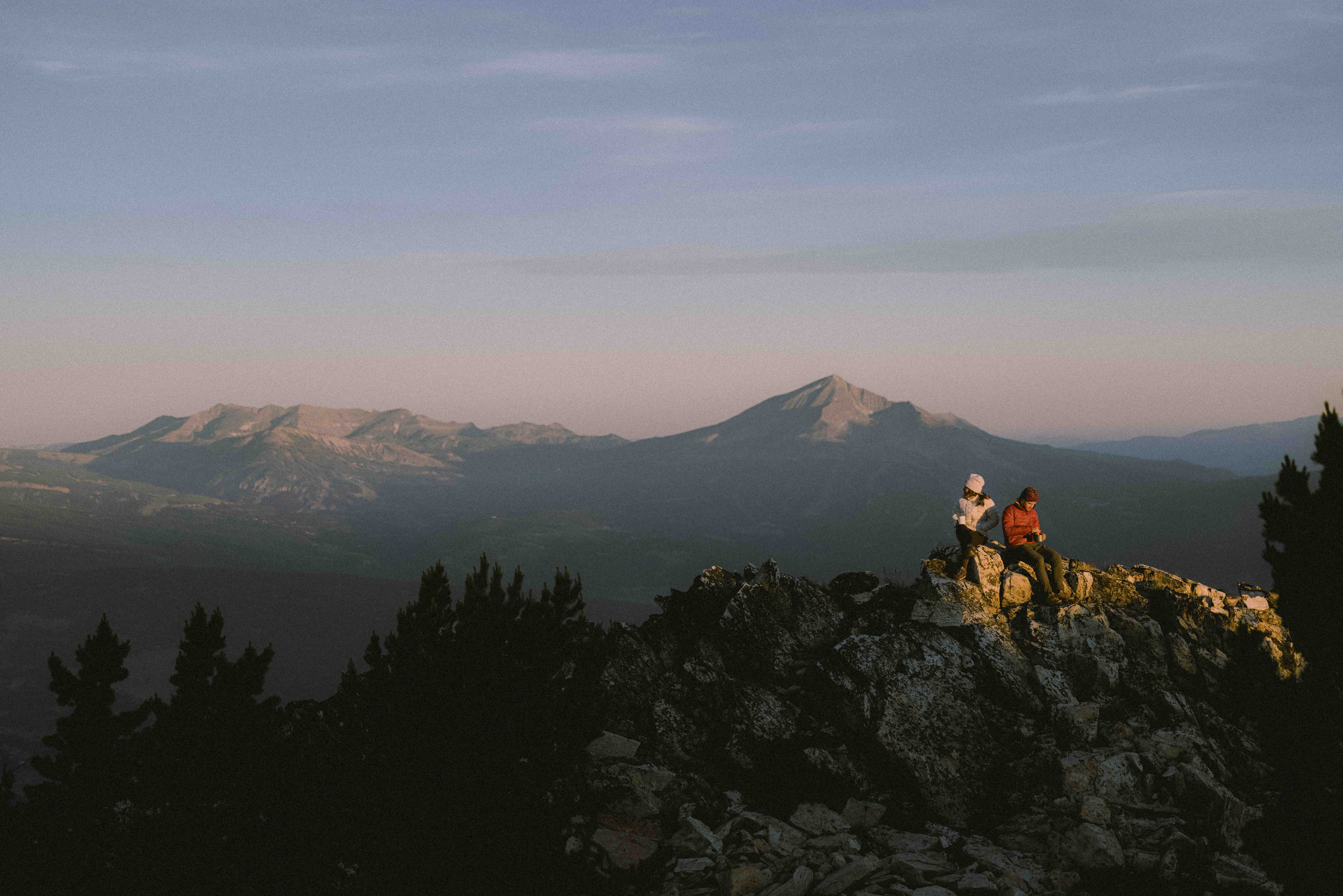 Two people hiking on a ridge at sunrise with mountains in the background.