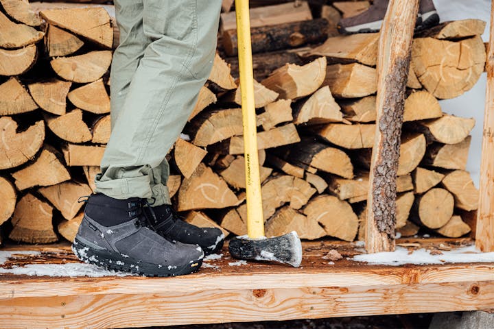 Man wearing Oboz snow boots while chopping firewood.