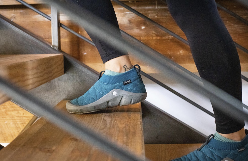 Woman walking up stairs at the Oboz office in Whakata Puffy sandals.