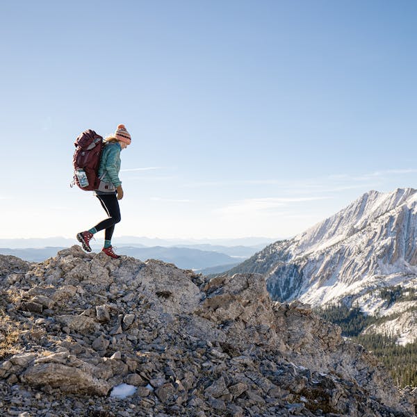 Woman wearing the rio red Bridger Mid Waterproof boots on a rocky outcrop in the snowy mountains.