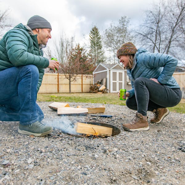 A couple prepares a campfire in their backyard while staying warm in Oboz winter boots.