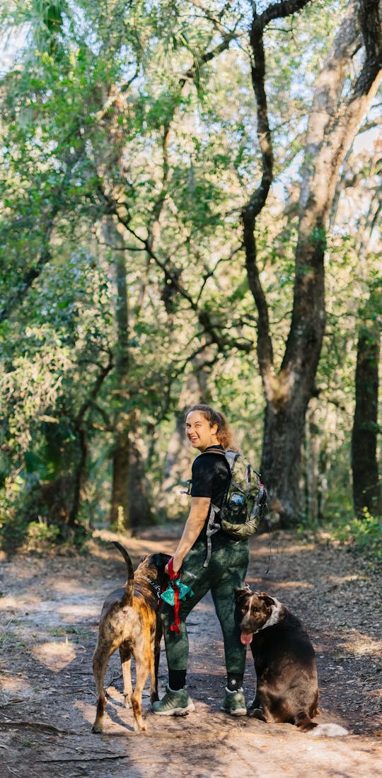 Woman hiking on a shady trail in Oboz Sypes Mid Leather B Dry hiking boots with two dogs