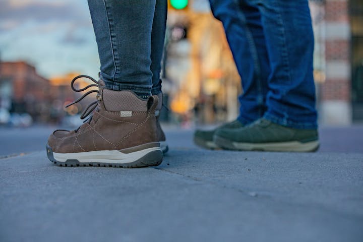 A couple in Oboz winter boots wait at a city crosswalk.