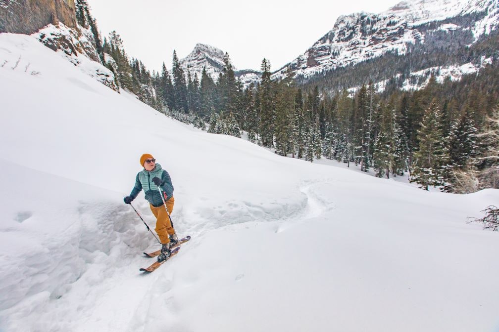 A skier in the Montana back country traverses snowy terrain using approach skis to access terrain. 