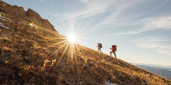 Two hikers scaling a grassy face in a bright afternoon.
