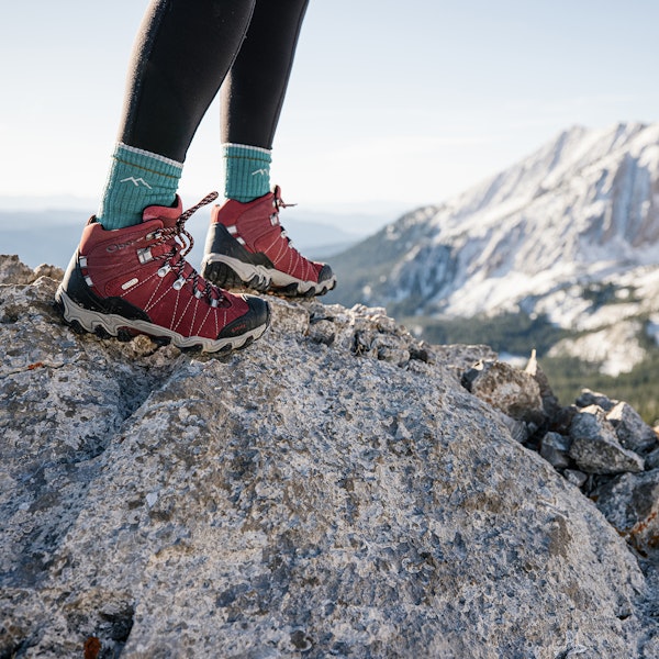 Close up view of the rio red Bridger Mid Waterproof boots on a rocky outcrop in the snowy mountains.