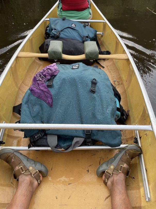 Person wearing Oboz trail sandals on a canoe filled with gear. 