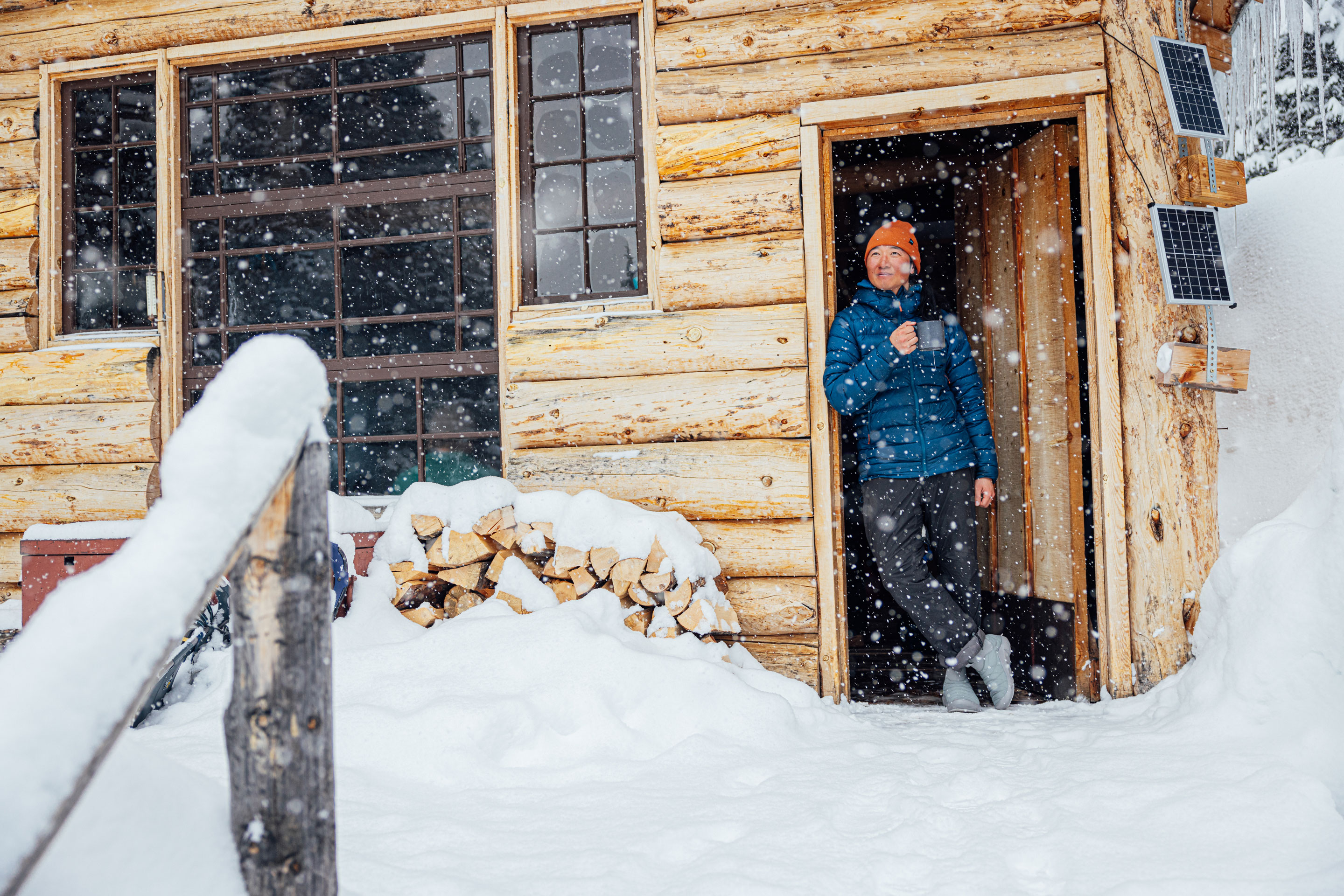 Man stands in doorway of log cabin wearing Oboz Whakatā Puffy Mid slipper shoes.