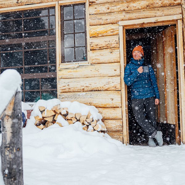 Man stands in doorway of log cabin wearing Oboz Whakatā Puffy Mid slipper shoes.