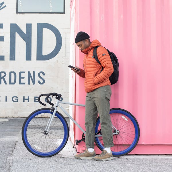 Man leans against a bright wall with his bike, wearing Oboz Beall casual shoes.