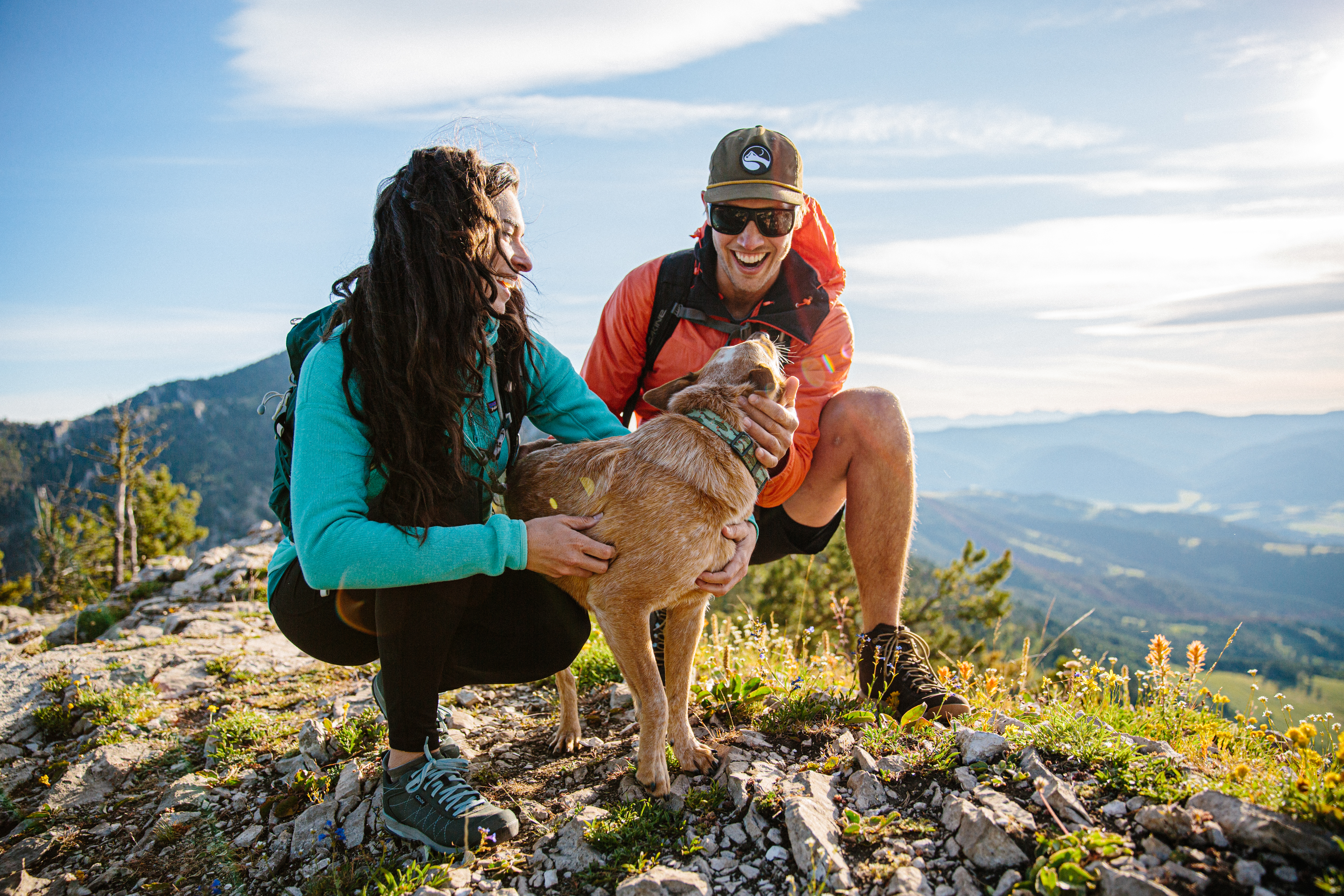 Two hikers wearing their Oboz hiking shoes stopped on a trail to pet a dog