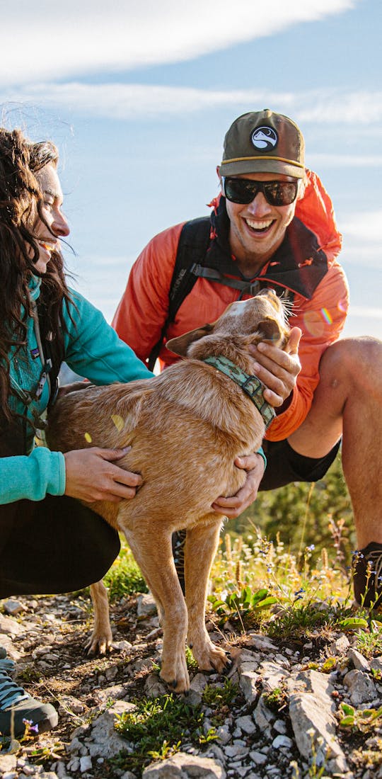 Two hikers wearing their Oboz hiking shoes stopped on a trail to pet a dog