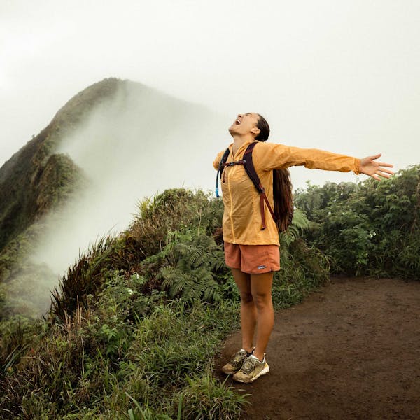Woman on top of a mountain peak in Hawaii after climbing a muddy mountainous trail.