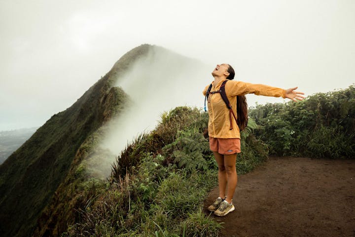 Woman on top of a mountain peak in Hawaii after climbing a muddy mountainous trail.