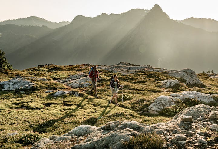 Two backpackers hike through a rocky field in the mountains.