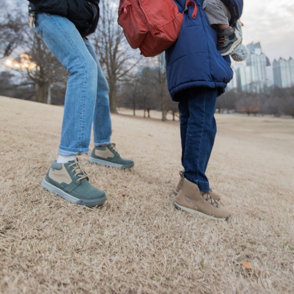 Man and woman stand in a field with a child wearing Oboz Burke Chukka and Hazel shoes
